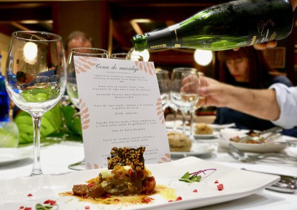 Vertido de espumoso Corpinnat en una copa durante una cena de maridaje, con la carta de platos y vinos visible en la mesa.